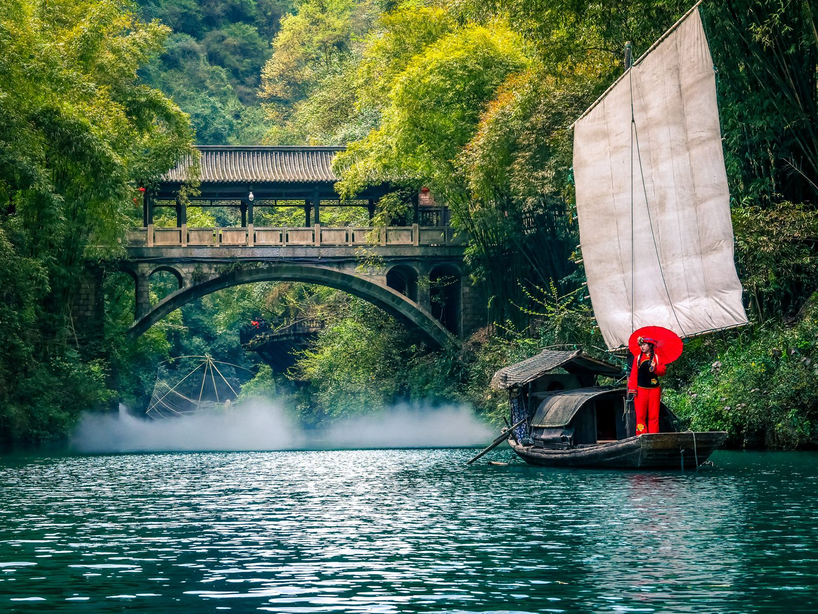 Wooden sailing junk with a red-clad boatwoman on a jade-green river gorge near Yichang, China, the kind of scene the best river cruises in Asia are built around