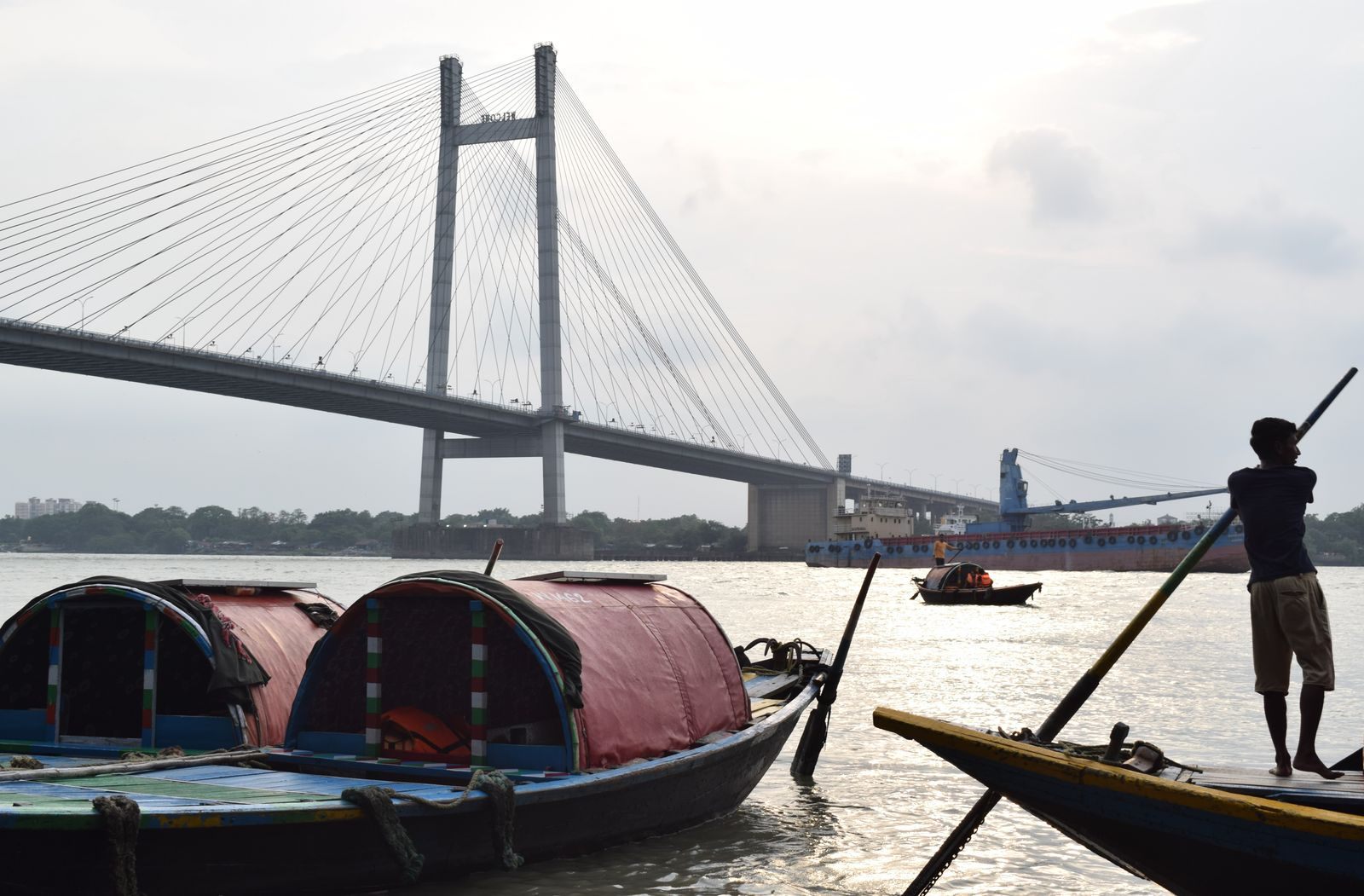 Boatman poling a covered country boat on the Hooghly in Kolkata beneath the Vidyasagar Setu bridge